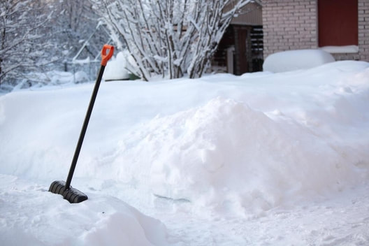 A shovel rests in a snowbank after being used to remove the snow from the sidewalk.